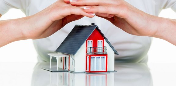 Hände halten schützend ein Modellhaus