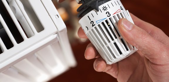 Hand stellt ein Heizkörper-Thermostat ein