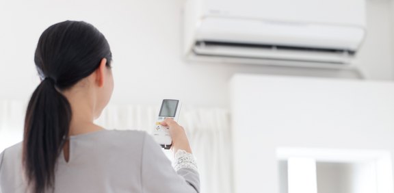 Frau steuert eine Wand-Klimaanlage mit der Fernbedienung