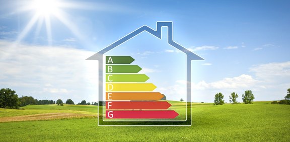 Haus-Symbol mit Energieeffizienzskala über grüner Wiese.