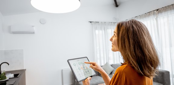 Frau steuert Klimaanlage bzw. Smart Home mit Tablet im Wohnzimmer