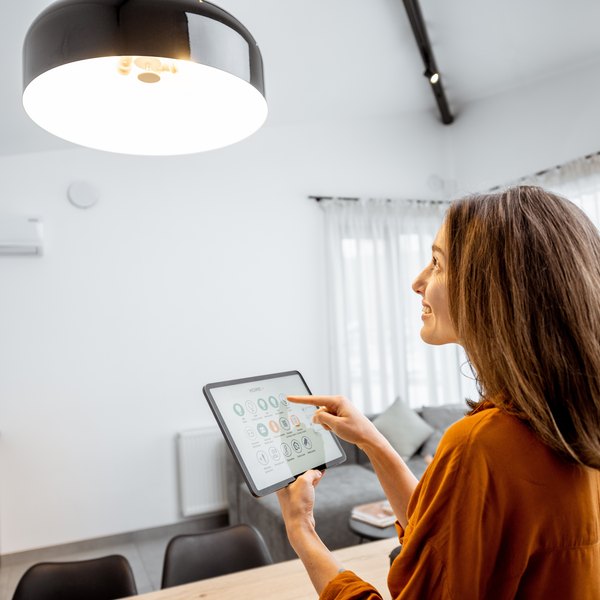 Frau steuert Klimaanlage bzw. Smart Home mit Tablet im Wohnzimmer