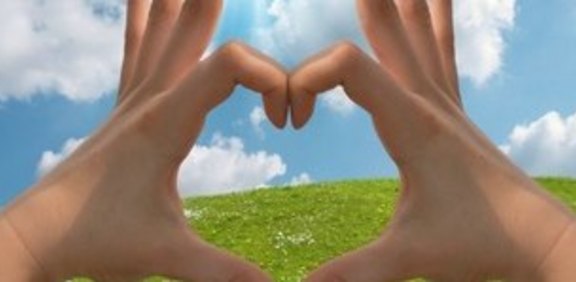 Hände formen ein Haus vor Wiese und blauem Himmel