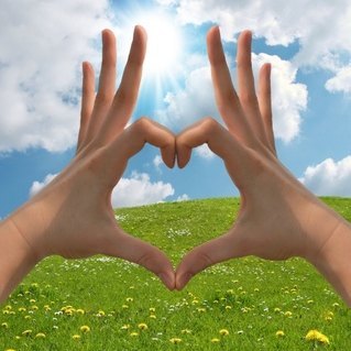 Hände formen ein Haus vor Wiese und blauem Himmel