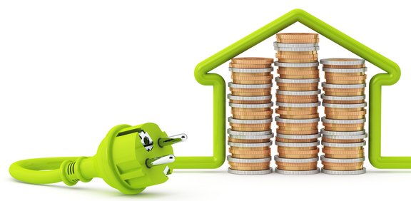 Grüner Stromstecker vor Münzstapeln in Hausform