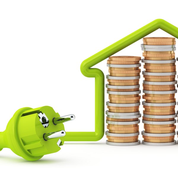 Grüner Stromstecker vor Münzstapeln in Hausform