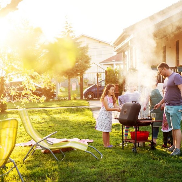 Familie grillt im sonnigen Garten vor dem Haus