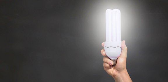 Hand hält leuchtende Energiesparlampe vor dunklem Hintergrund