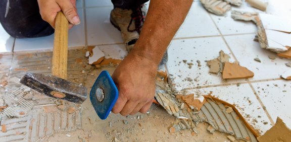 Fliesen werden mit Hammer und Meißel vom Boden entfernt.