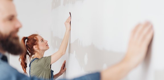 Paar spachtelt oder schleift eine Wand bei der Renovierung.