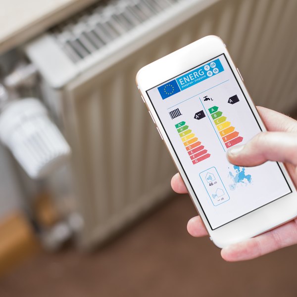 Smartphone mit Energie-App vor einem Heizkörperthermostat