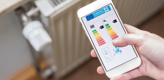 Smartphone mit Energie-App vor einem Heizkörperthermostat