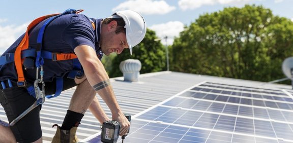 Monteur montiert Solarmodule auf einem Dach mit Akkuschrauber