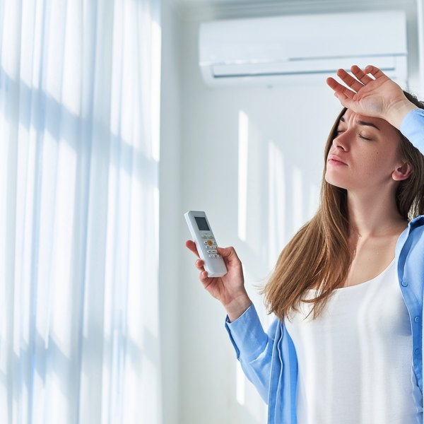 Frau mit Fernbedienung steht unter Klimaanlage und wischt sich die Stirn