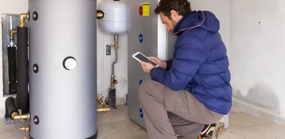 Techniker prüft mit Tablet einen großen Heizspeicher im Technikraum